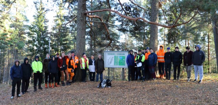 Iso ryhmä ihmisiä poseeraa rivissä metsän reunalla.