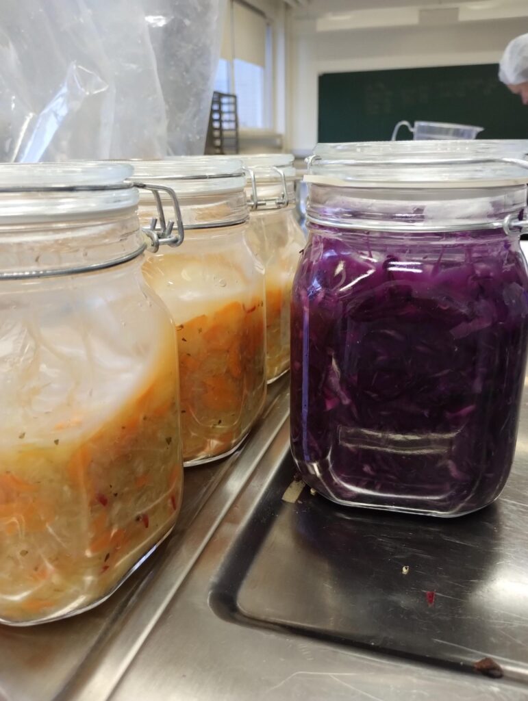 Lasipurkkeja, joissa on fermentoituja kasviksia valmiina.