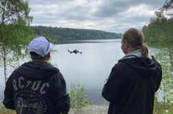 kaksi miestä lennättää dronea järven rannalla