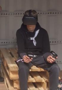 Henkilö istuu penkillä virtuaalilasit päässä ja ohjaimet kädessä