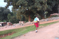 Poika kävelee reppu selässään afrikkalaisella kylätiellä