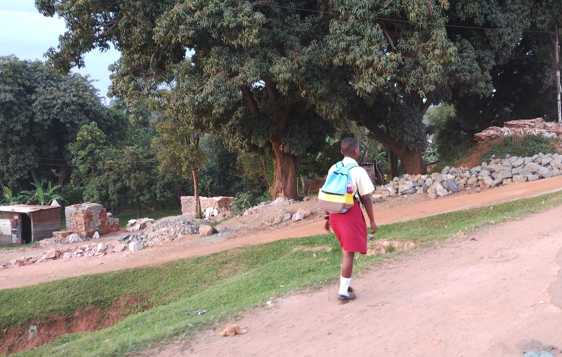 Poika kävelee reppu selässään afrikkalaisella kylätiellä