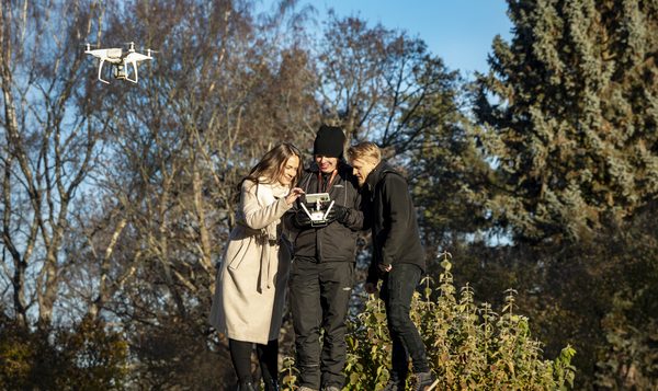 Kolme ihmistä tarkastelee dronea syksyisessä maisemassa.