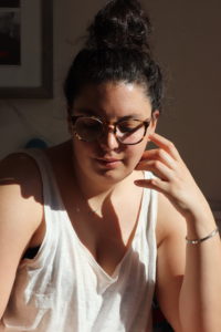 Portrait of Isabel. Isabel has dark hair with a bun and black-brown glasses.
